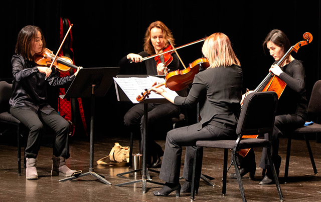 Four women playing stringed instruments sit in a circle