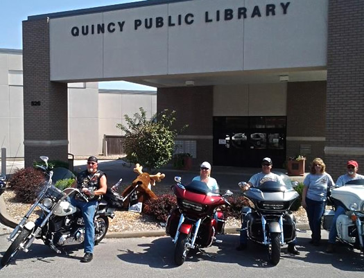 Group of adults astride their morcycles in front of the Quincy Public Library 