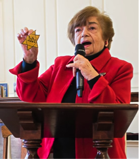 Older woman holding a six-sided yellow star speaking at a podium