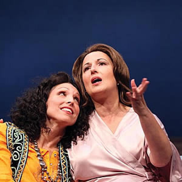 Two actresses - one expostulating the other next to her with head on shoulder 
