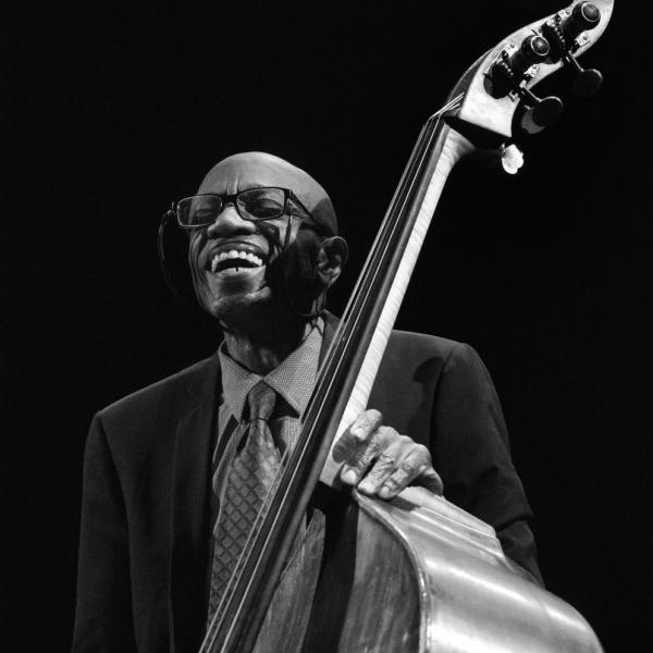 Man with glasses smiling holding an acoustic bass. 