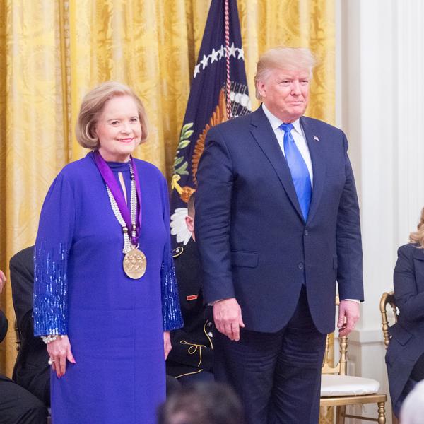Woman in purple stands next to president. 