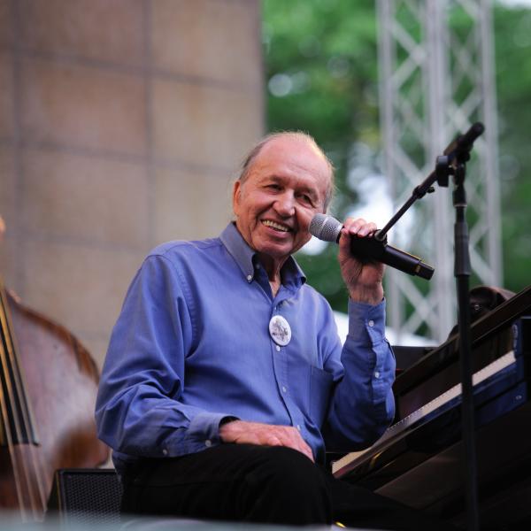 Man at piano on stage, smiling into camera.