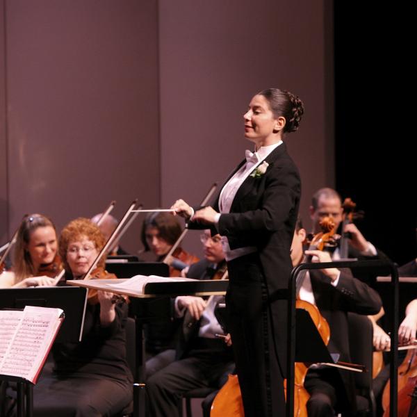 Woman in tux leading an orchestra. 