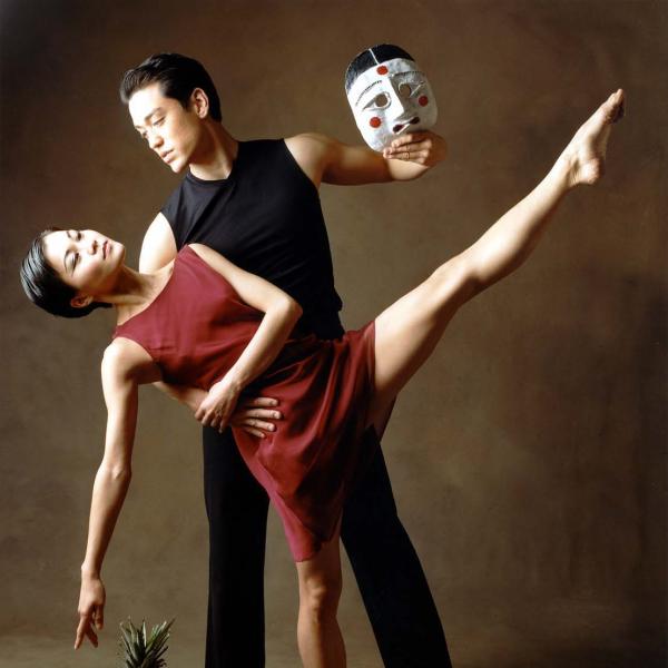Woman in red dancing with man in black hold a mask.
