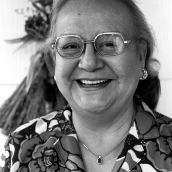 Older woman with long gray hair wearing glasses, smiling. 