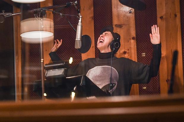 A person passionately singing into a suspended mic in a recording studio, hands in the air and eyes shut.