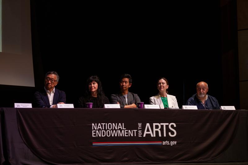 A group of 5 people sit behind a table with the National Endowment for the Arts logo