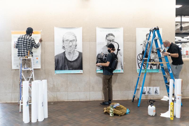 several people in a gallery space at work affixing portraits to the wall