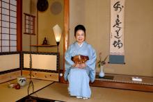 A woman in traditional Japanese clothing sits next to tea ware.