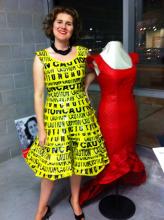 a woman wears a fitted dress made of caution tape and stands next to a dressmakers model wearing a red dress with a scalloped hi lo bottom