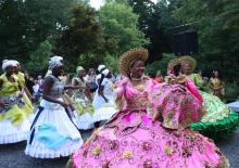 a parade of women in brilliantly colored costumes featuring wide hoop-like skirts that are heavily decorated