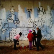 a man and three kids stand in front of the outline of a mural featuring robots 