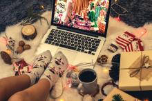 Photo of a laptop playing a Christmas movie surrounded by festive treats and feet in snowman socks