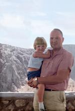 a man holds a small child in his arms in front of a mountainous landscape