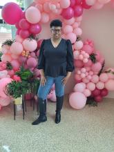a Black woman stands in front of an arch made of pink balloons