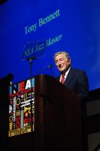 Tony Bennett stands smiling behind a lectern with the NEA Jazz Masters logo 