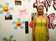 Philippa Highes in a yellow dress in front of a humorous wall art piece