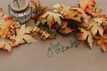 ribbon-like arrangement of fall leaves on a table with a votive candle and Give Thanks handwritten in script