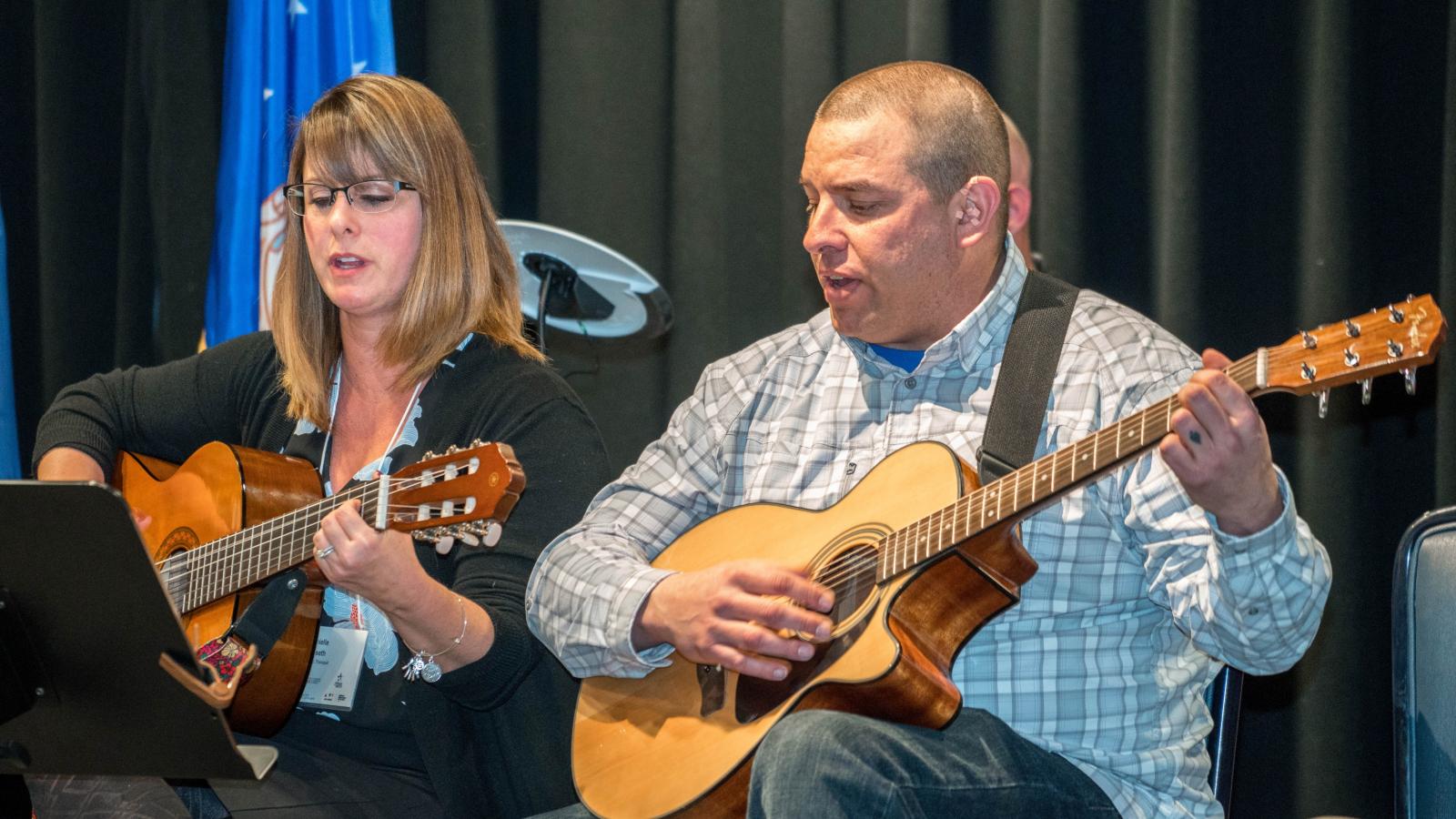 woman and man sitting down playing guitar together