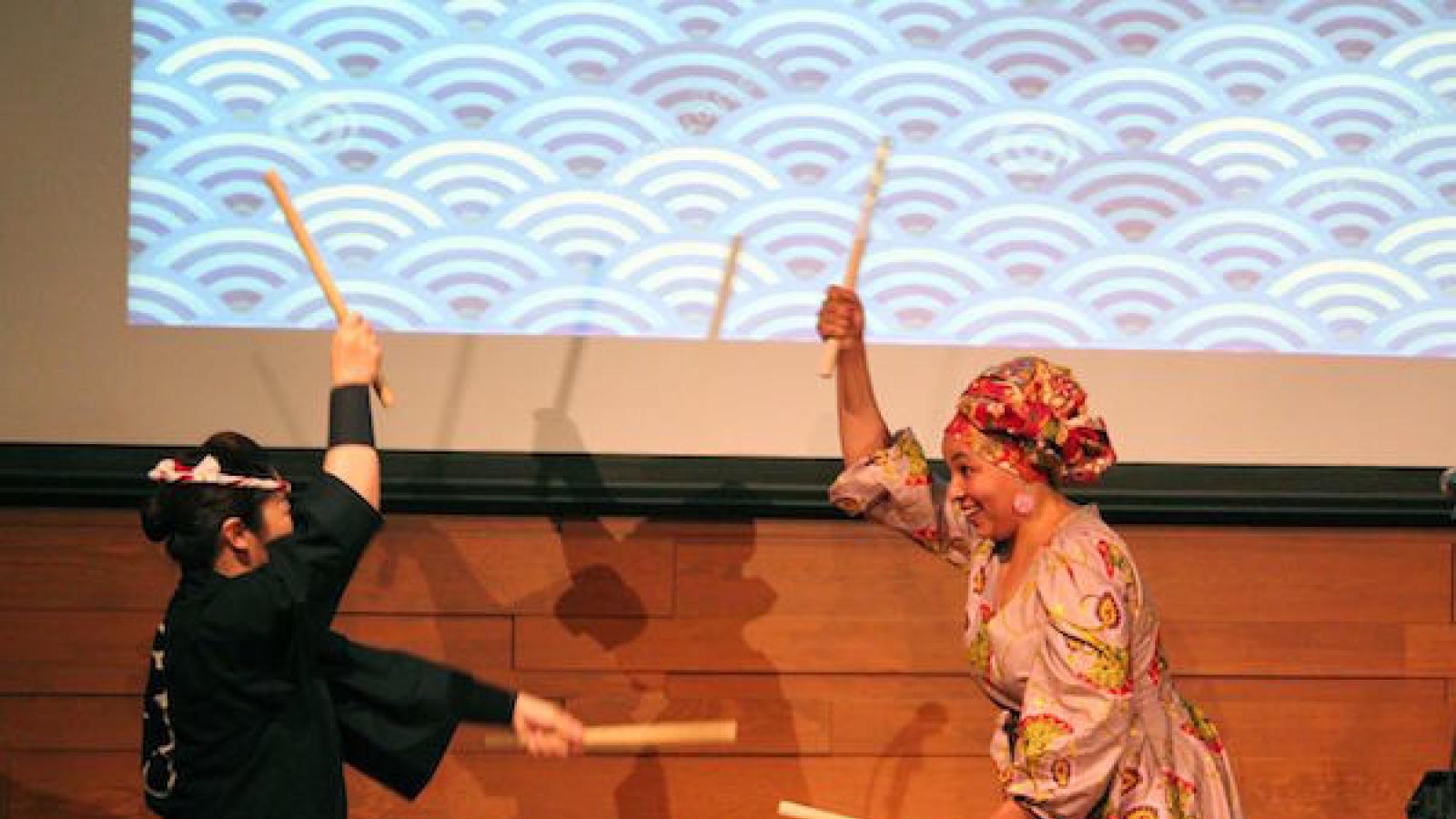 two women play a taiko drum standing on either side of it