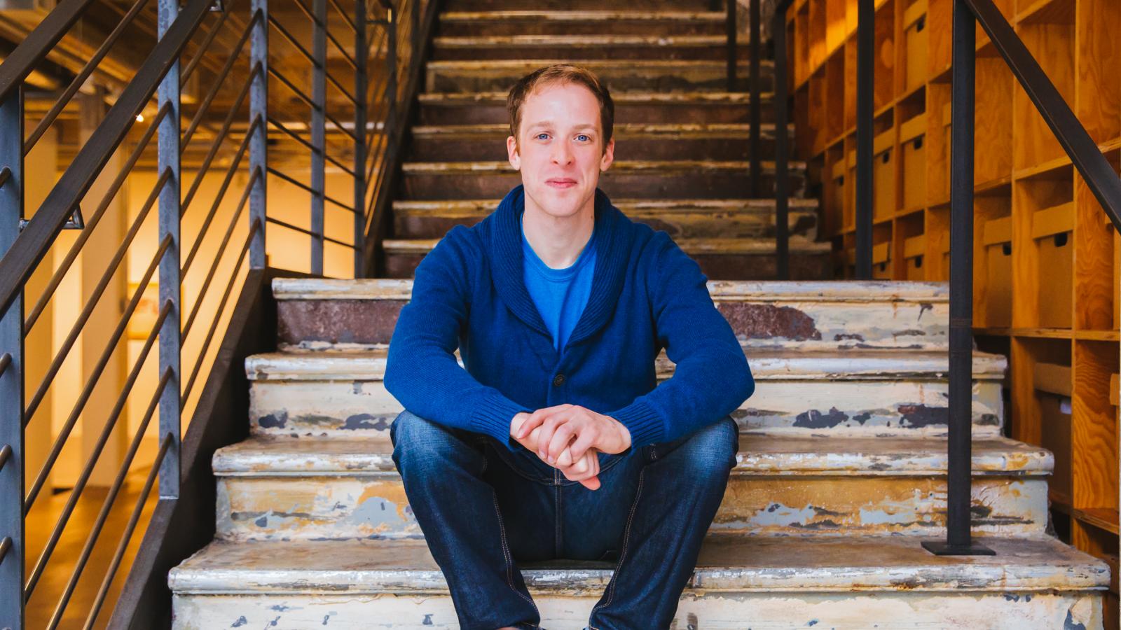 Man in blue shirt sitting on steps and looking at camera
