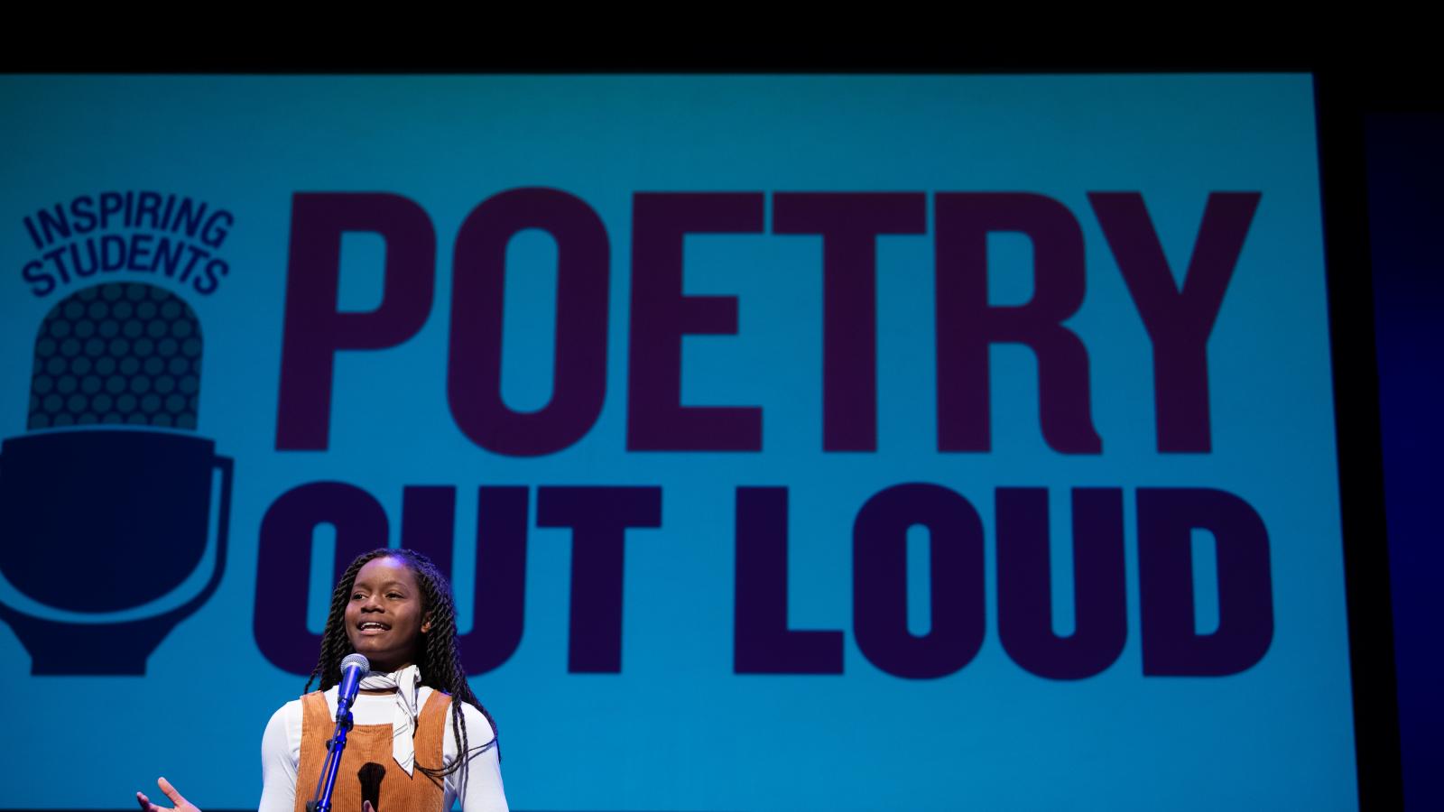 A young woman speaks at a microphone with the Poetry Out Loud logo on a screen behind her.